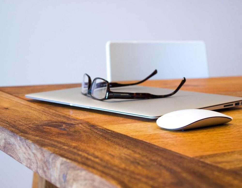 A laptop and a pair of reading glasses on a wooden desk